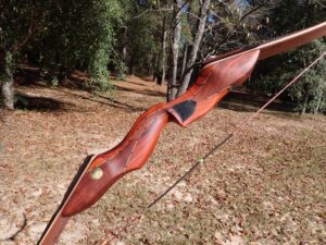 A handcrafted wooden recurve bow displayed outdoors on a sunny day.