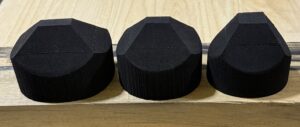 Three black, polygonal objects on a wooden surface.