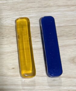 Two rectangular resin or plastic blocks, one amber and one dark blue, on a wooden surface.