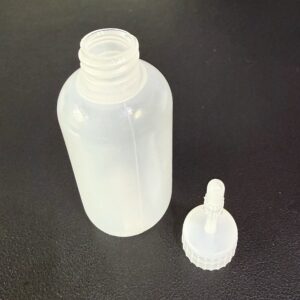 A clear plastic bottle with a separate dropper cap on a black surface.