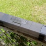 A closed black rifle case resting on a wooden surface outdoors.