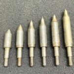 A set of six metallic pointed weights arranged by size on a grey surface.