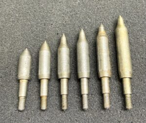 A set of six metallic, bullet-shaped objects arranged by size on a gray surface.