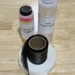 Two bottles and two rolls of tape on a wooden surface.