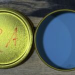 Open metal container with a yellow lid and blue interior on a wooden surface.