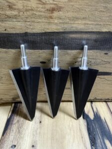 Three black metal arrowheads with threaded shafts on a wooden surface.