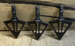 Three black broadhead arrow tips on a wooden surface.