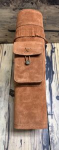 Brown suede pouch with button closure on a wooden surface.