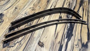 Two sleek black windshield wiper blades on a wooden surface.
