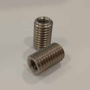 Two metal threaded inserts on a plain surface.