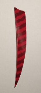 A red feather with dark zigzag patterns against a plain background.