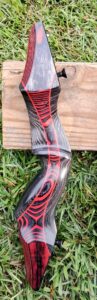Close-up of a colorful archery bow on grass and wood.