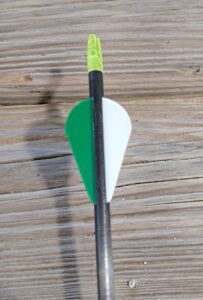 Close-up of an arrow with green and white fletching on a wooden surface.