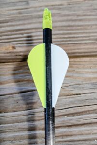 Close-up of an arrow shaft with yellow and white fletching on a wooden surface.