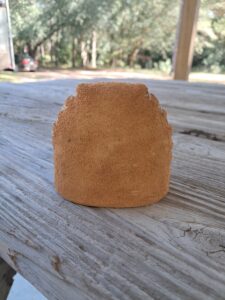 A small, rough-textured brown rock on wooden surface outdoors.