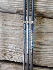 Three golf club shafts with labels on a wooden surface.