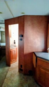 View of a partially open wooden door leading to a bathroom with sink and mirror.