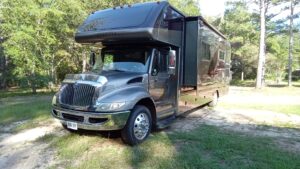 A large black motorhome parked on grass near trees.