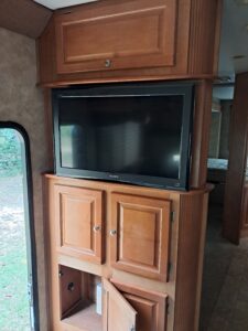 Flat-screen TV mounted above wooden cabinets in an RV interior.