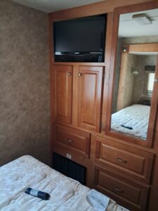 Cozy RV bedroom corner with TV, wooden cabinets, and mirrored wardrobe.