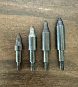 Four metal drill bits of varying sizes arranged on a wooden surface.