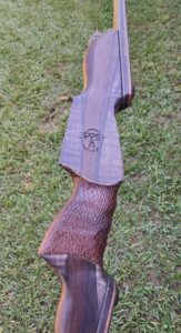 Close-up of a wooden rifle stock with a textured grip on grass.