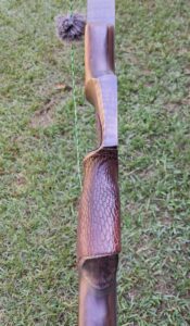 Handmade wooden bow with textured grip placed on grass.