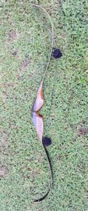 A traditional wooden bow with a string lying on grass.