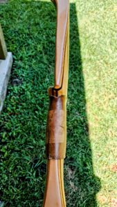 Close-up of a wooden rifle stock on grass.