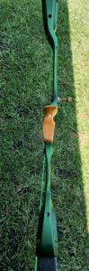 A green and wood recurve bow lying on grass.