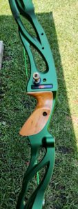 Close-up of a green and wooden archery bow handle lying on grass.