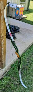 A green recurve bow leaning against a wooden post outdoors.