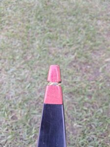 A red shuttlecock resting on a black badminton racket against a grass background.