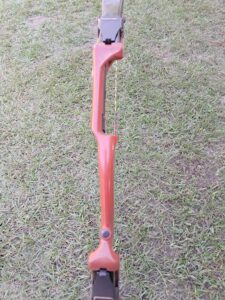 A red plastic archery bow frame lying on grass.