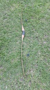 Traditional wooden recurve bow lying on green grass.