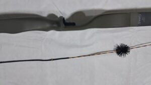 A rifle stock and a cleaning brush laid out on a white surface.