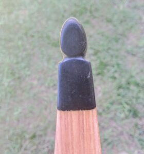 Close-up of a wooden arrow tip with a black rubber nock on grassy ground.