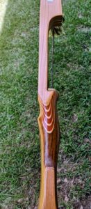 Close-up of a wooden rifle stock with layered wood design on grass.