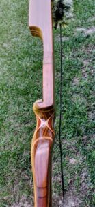 A handcrafted wooden bow lying on grass.