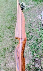A beautifully crafted wooden recurve bow resting on grass.