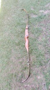 A traditional wooden bow lying on grass.