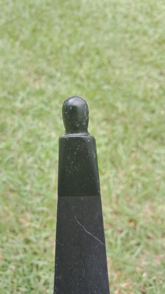 Close-up of a black post with a rounded top on grass.