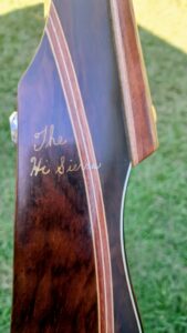 Close-up of a wooden guitar headstock with "The Heirloom" inscribed.