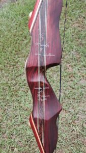 Close-up of a wooden archery bow with string and engraved text.