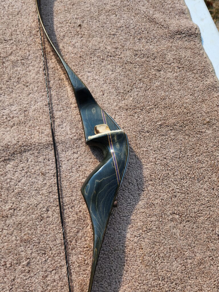A sleek black recurve bow lying on a brown textured surface.