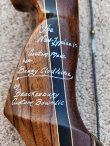 Close-up of a wooden rifle stock with white handwritten custom maker details.