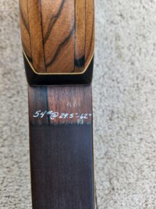 Close-up of a wooden bow limb with handwritten length and weight details.