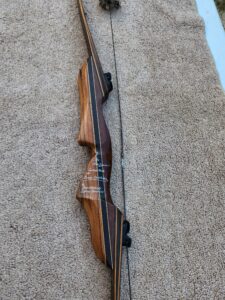 A wooden recurve bow with a taut string against a carpeted background.