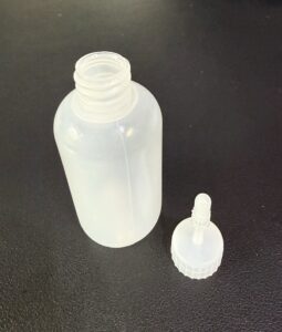A transparent plastic bottle with a separate dropper cap on a black surface.