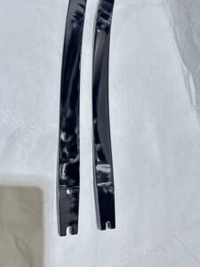 Two black metal strips with curved and notched ends on a white fabric background.